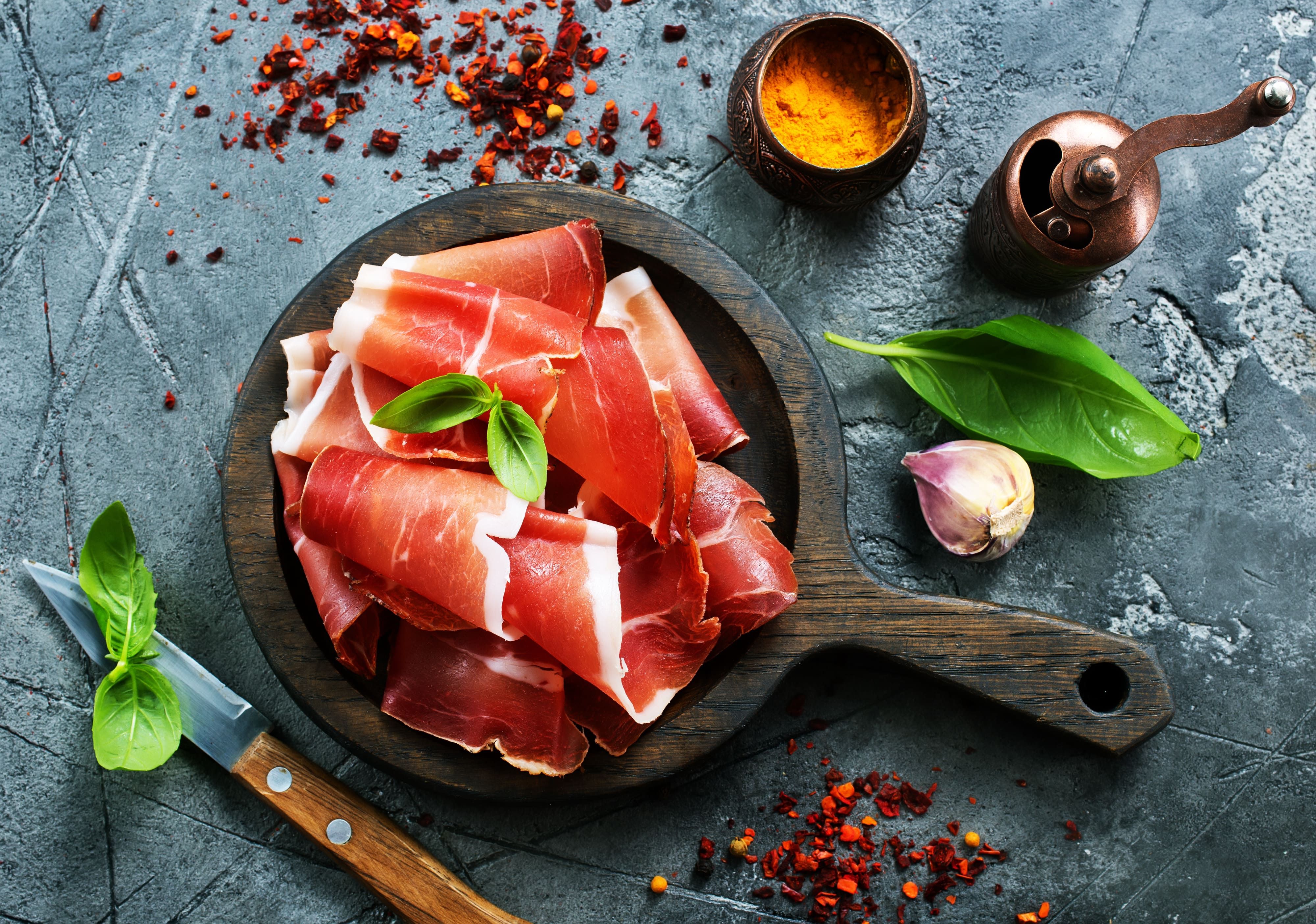 Ein Holzschneidebrett mit Scheiben Fleisch und Kräutern - Bild auf vieni.ch