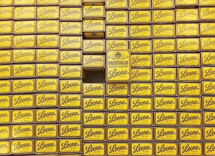 Wand aus gelben Schachteln der Marke Leone, eine Schachtel zeigt 'PASTIGLIE DIGESTIVE DISSETANTI' und das Gründungsjahr…