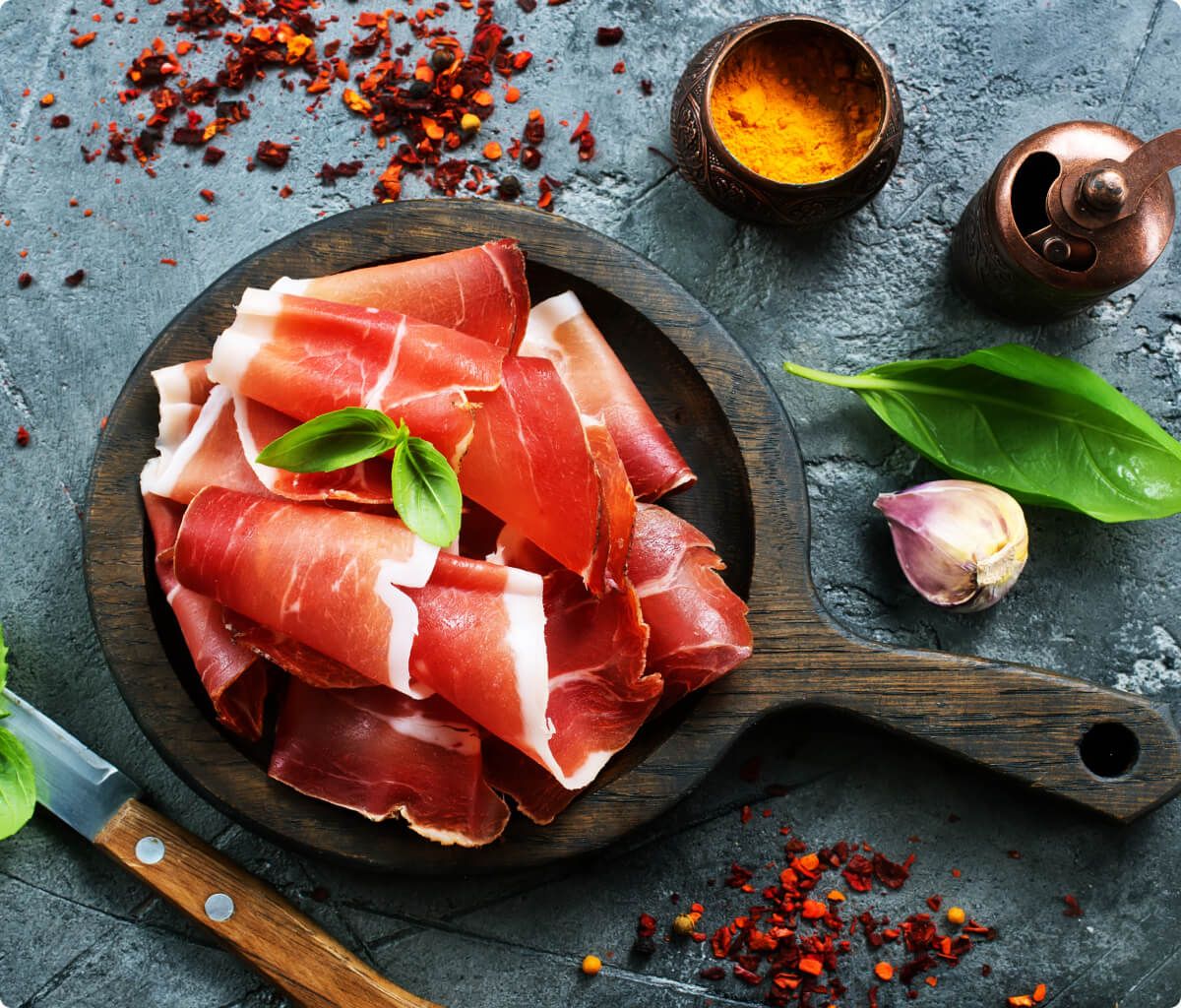 Italienischer Prosciutto Rohschinken in dünnen Scheiben auf einem Holzbrett angerichtet – klassische italienische Antipasti