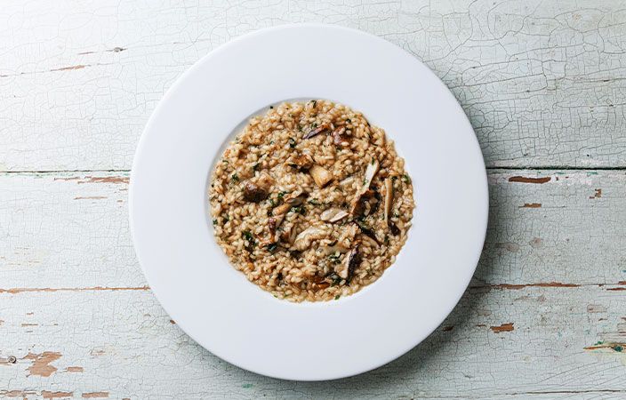 Ein weisser Teller mit einer Schüssel Pilzrisotto  Bild auf vieni.ch