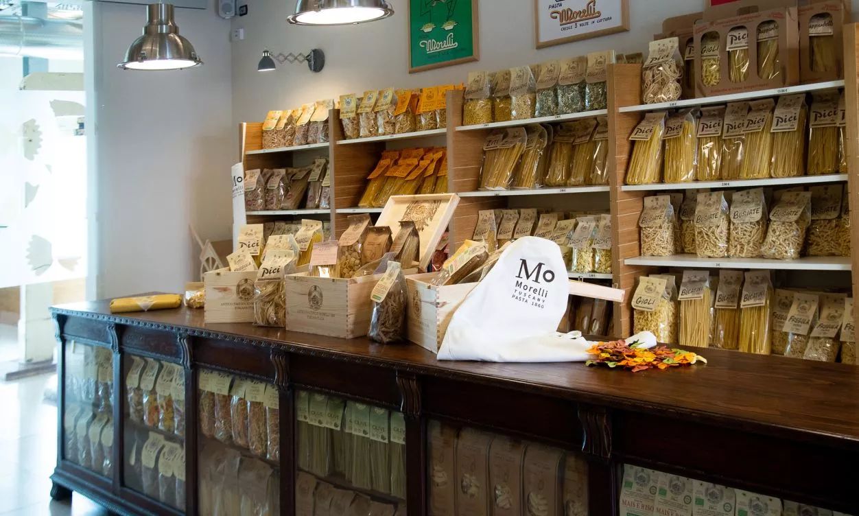 Pasta-Shop mit Holztheke und Regalen voller verpackter Pasta, darunter Morelli, Pici und bunte Nudeln.