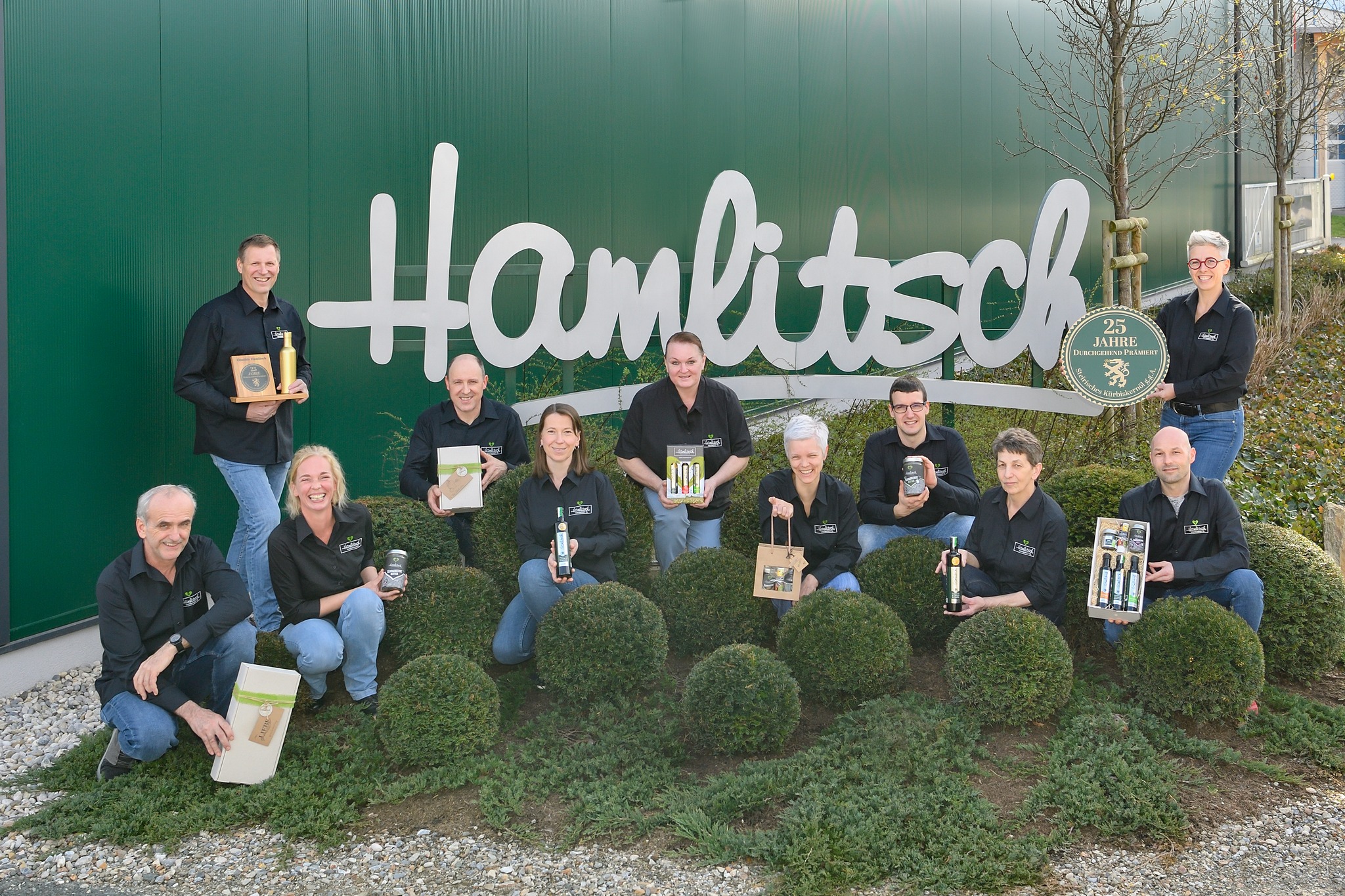 Team von Hamlitsch posiert vor dem Firmengebäude mit Produkten und einem Schild zum 25-jährigen Jubiläum.