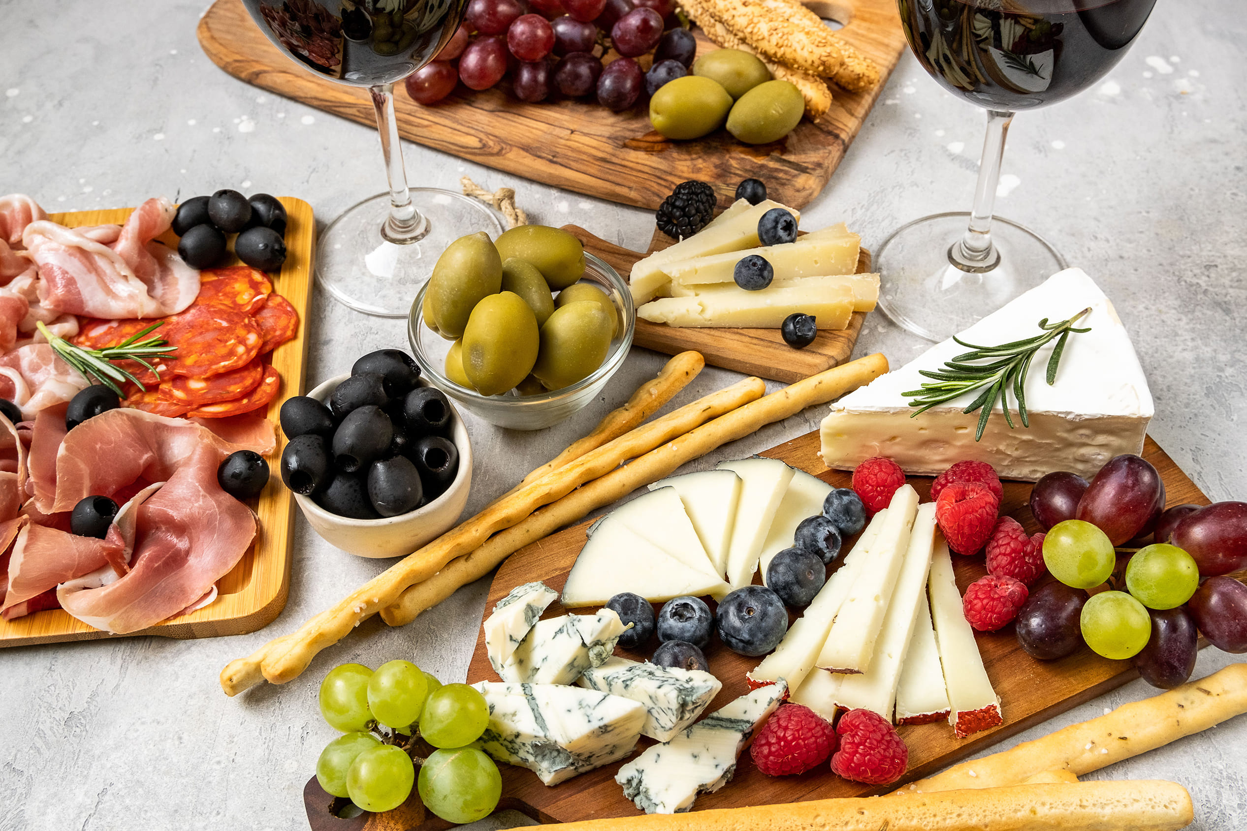 Apero-Platte mit verschiedenen Käsesorten, Aufschnitt, Oliven, Trauben, Beeren und Grissini, dazu zwei Gläser Rotwein.