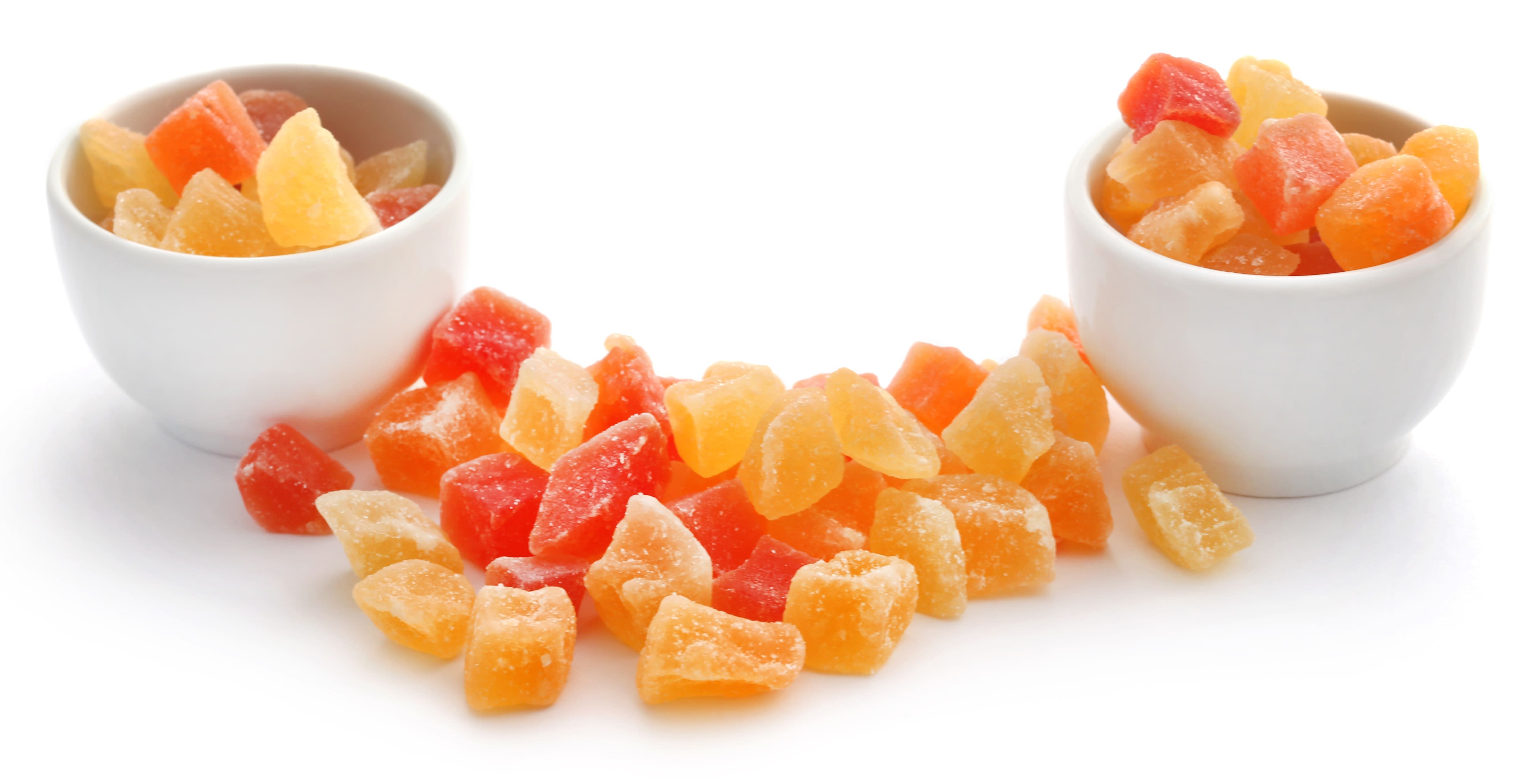 Getrocknete, gezuckerte Fruchtwürfel in Rot-, Orange- und Gelbtönen, teils in zwei weissen Schalen, teils verstreut.